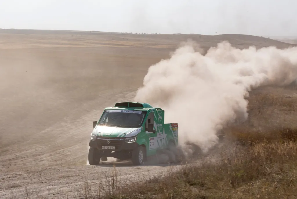 зелёный внедорожник едет по песчаной дороге
